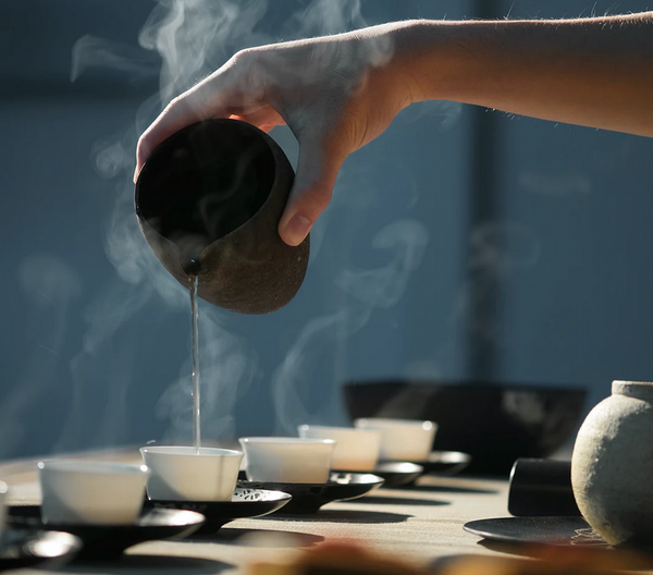 A hand pouring tea into small cups